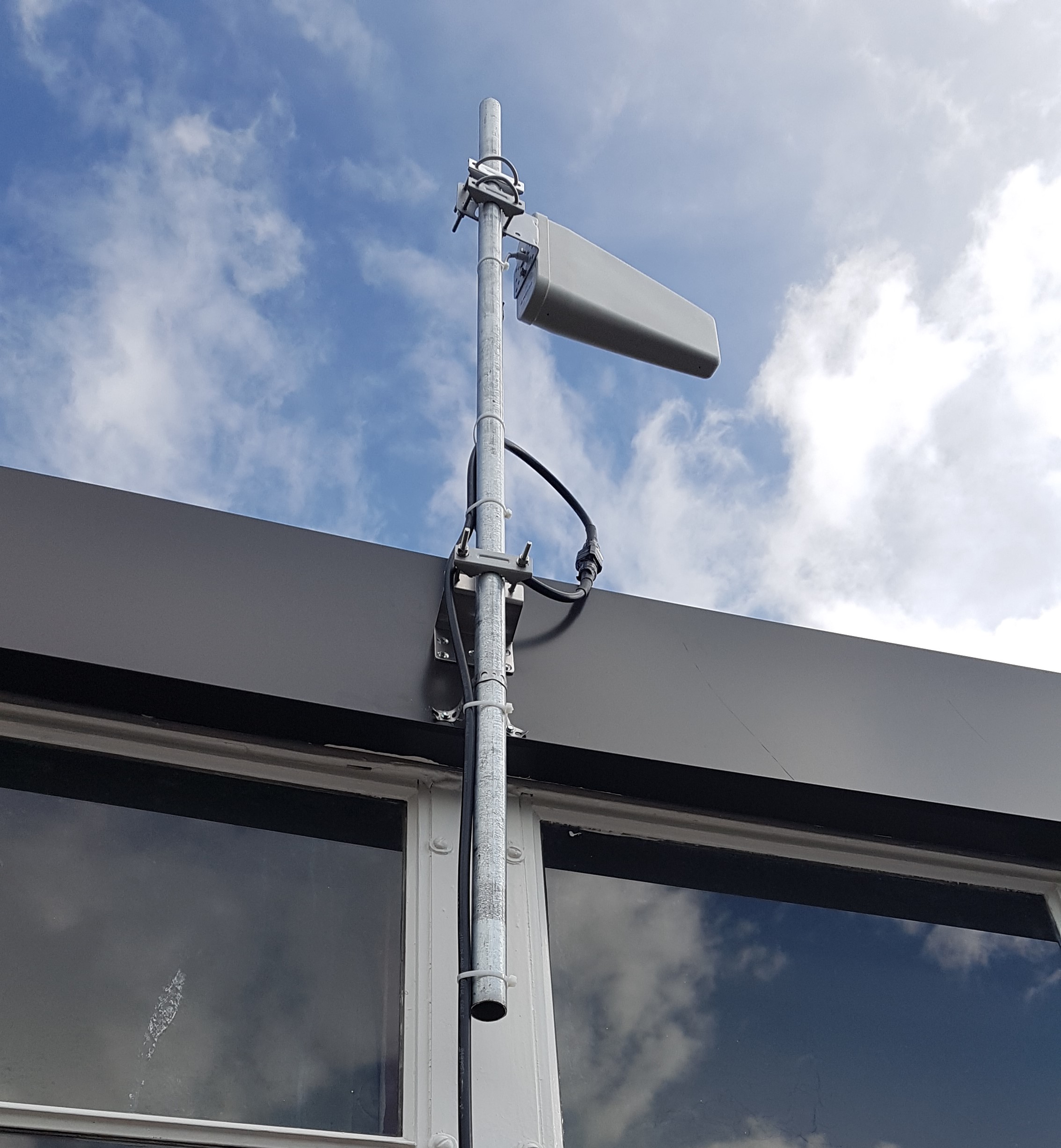 Cellular signal booster antenna mounted on an exterior mast with secured coaxial cable